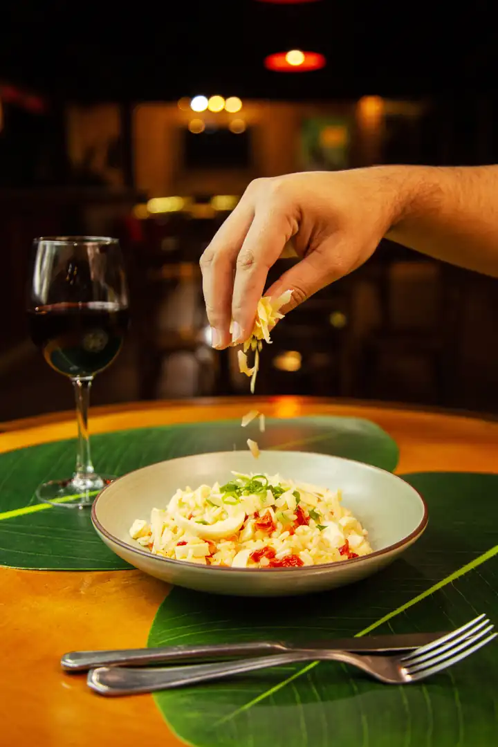 Risoto finalizado com queijo ao lado de uma taça de vinho